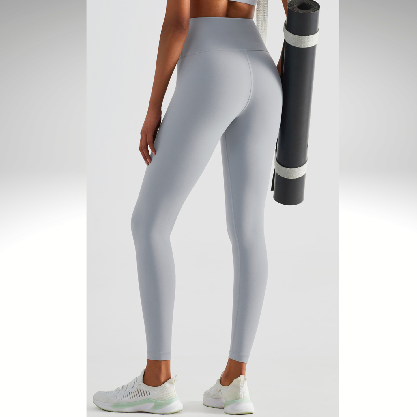 Person wearing gray leggings holding a black and white yoga mat on a light gray background
