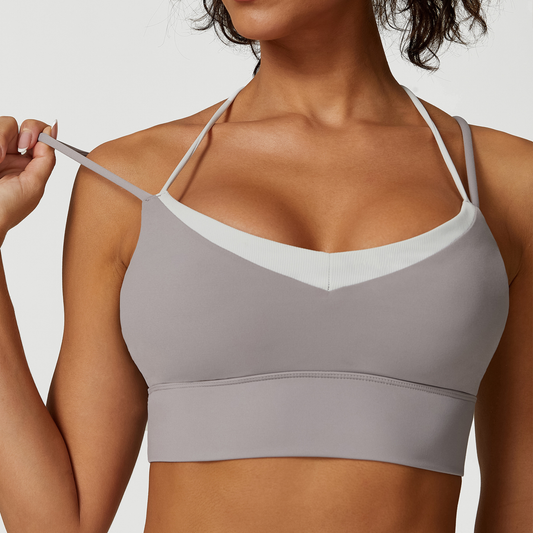 Woman wearing a gray sports bra with white straps on a plain background
