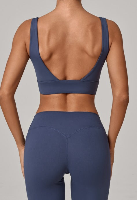 Rear view of a model wearing a navy blue sports bra and matching high-waisted leggings against a solid gray background.