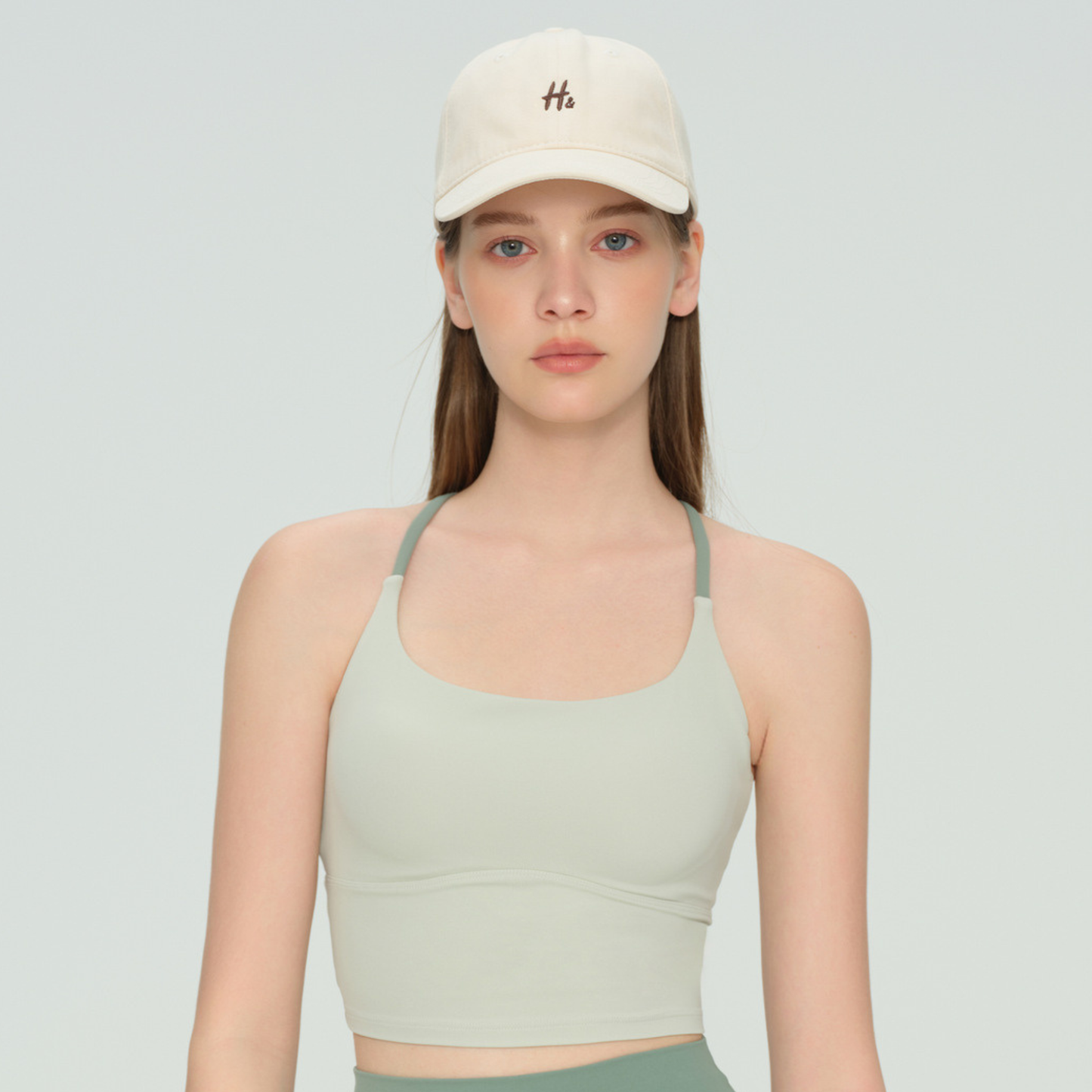 Woman wearing a beige cap and green sports bra on a light gray background