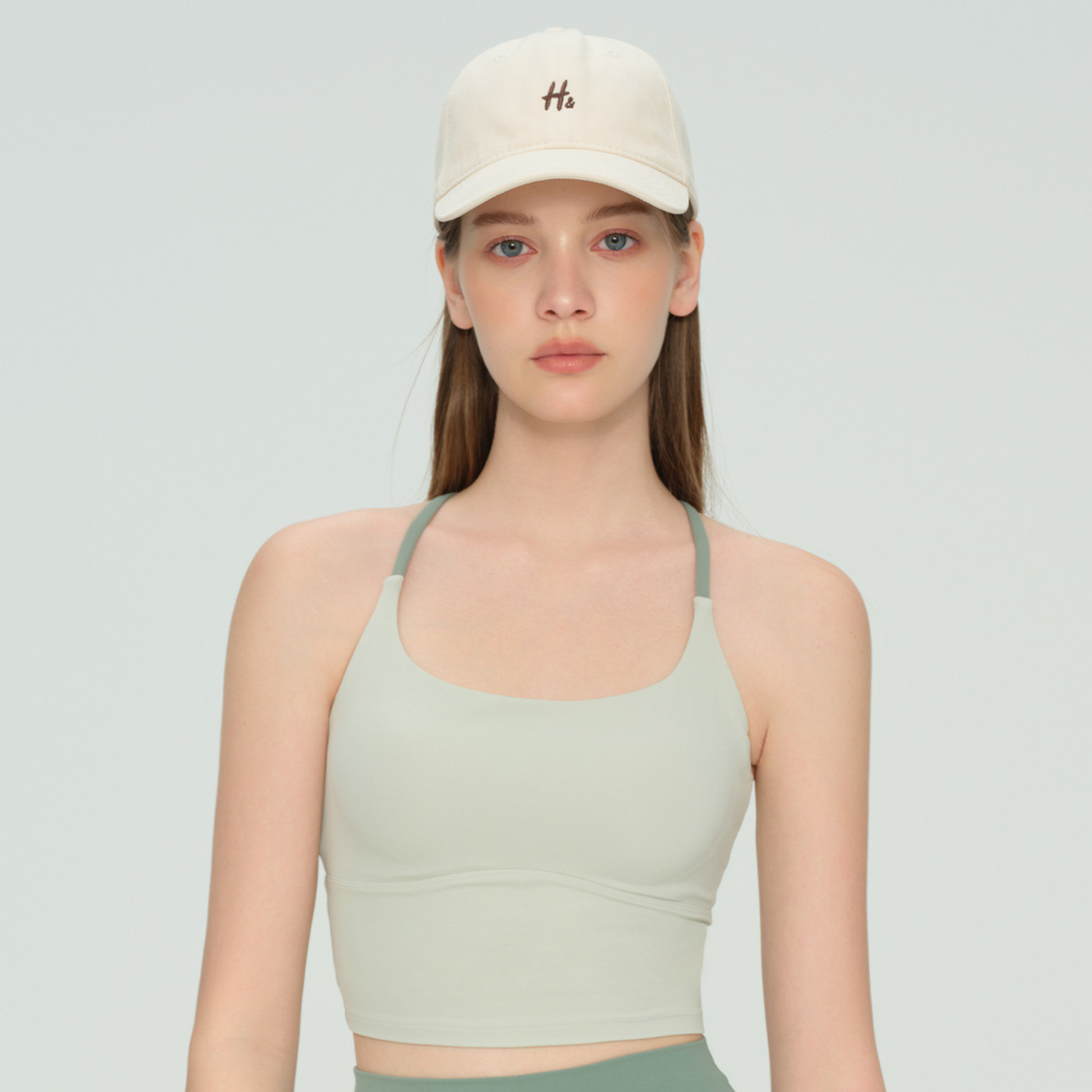 Woman wearing a beige cap and green sports bra on a light gray background