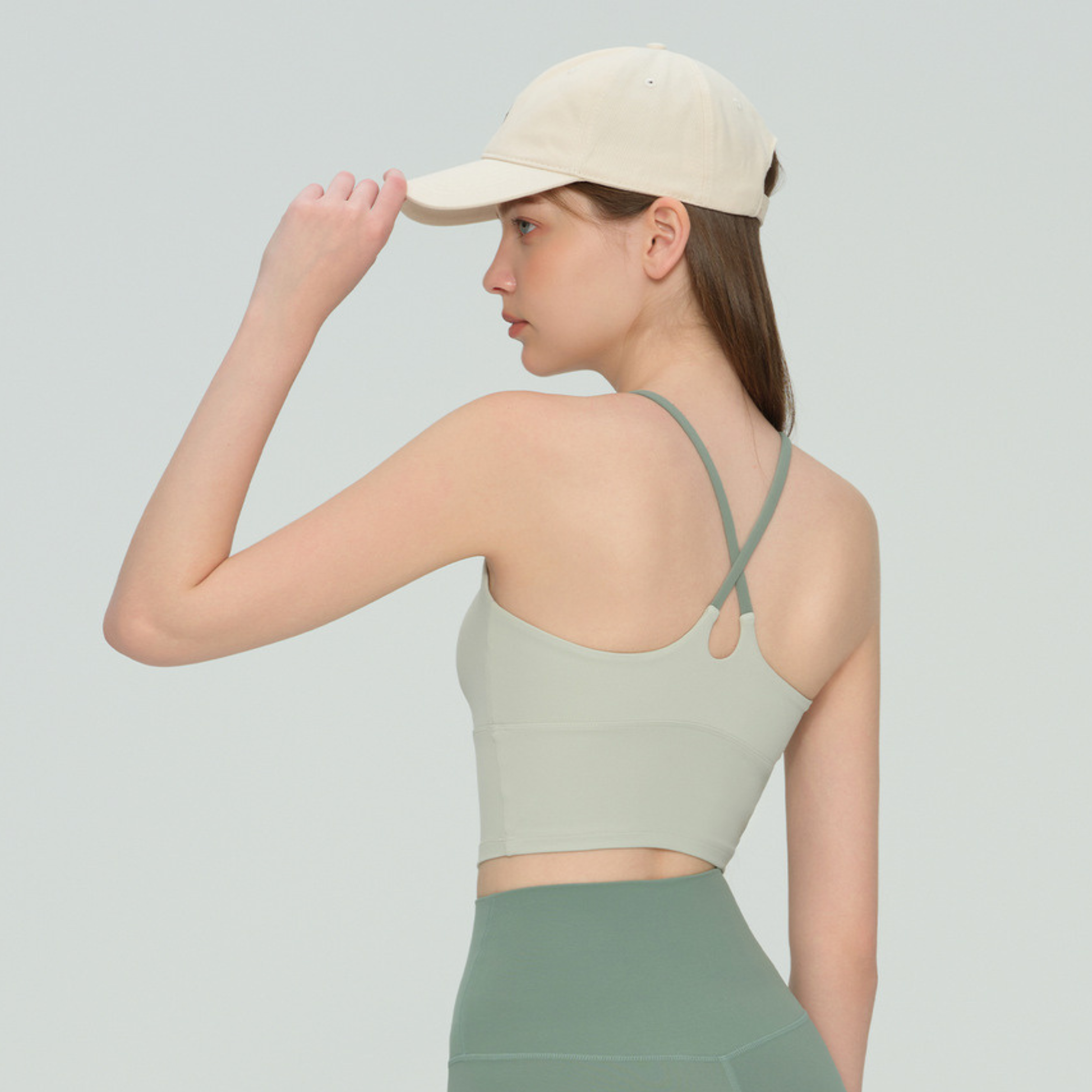 Woman wearing a light green sports bra and cap on a plain background