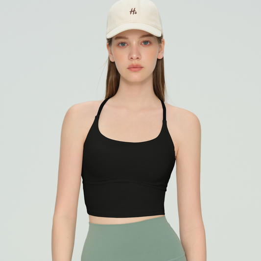 Woman wearing a black sports bra and beige cap on a light gray background