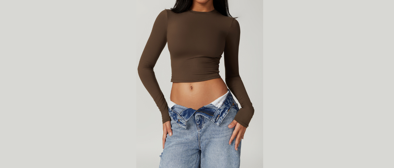 Person wearing a brown long-sleeve crop top and blue jeans on a plain background