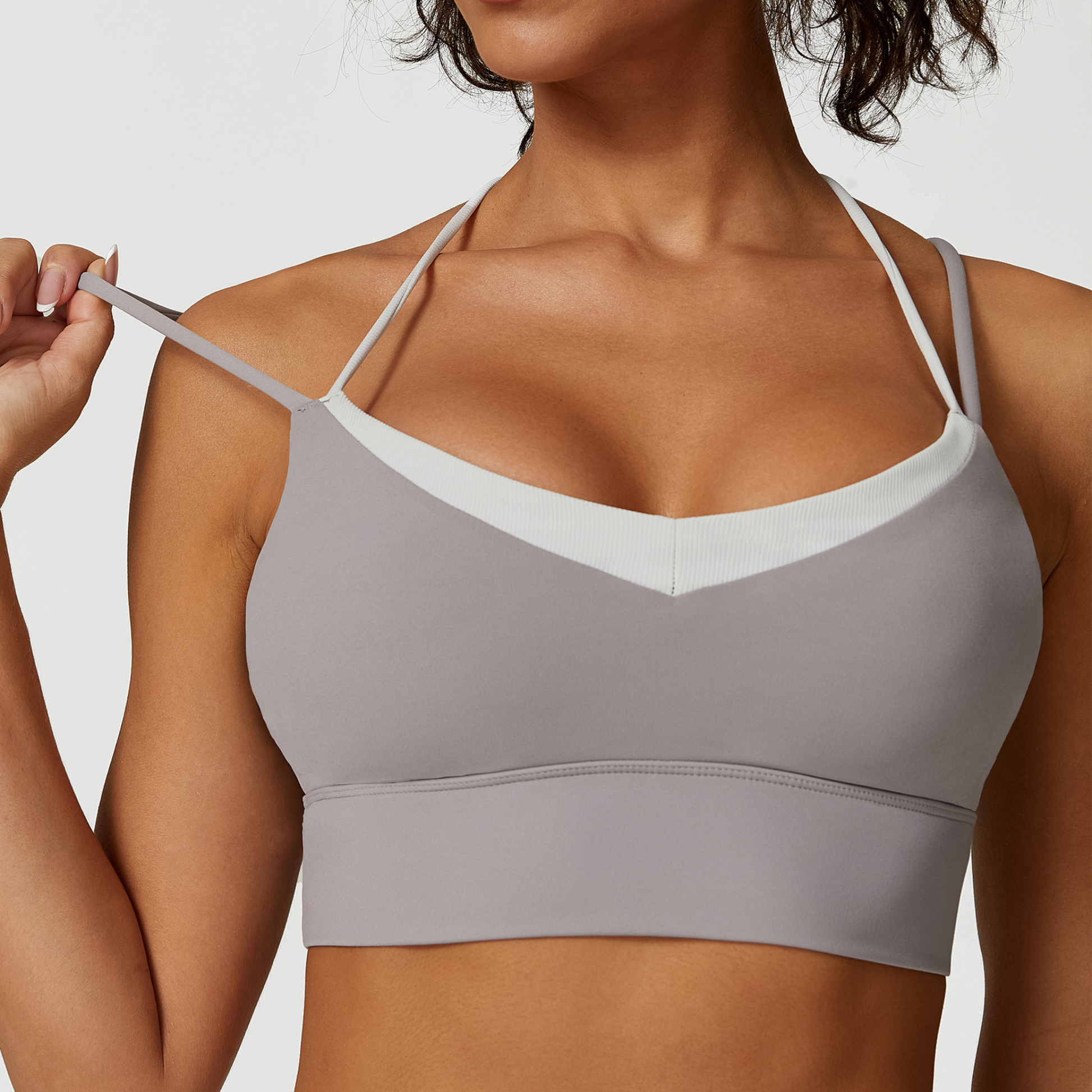 Woman wearing a gray sports bra with white straps on a plain background
