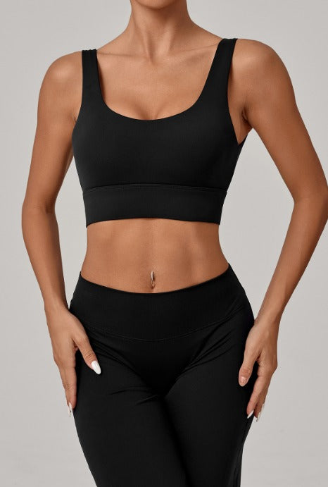 A woman wearing a black sports bra and matching black high-waisted leggings against a solid light gray studio background.